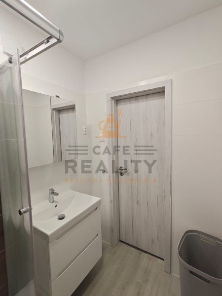 Na prenájom 1 izbový byt, 34 m2, Bratislava, Petržalka, Lachova ulica - Kúpeľňa v 1-izbovom byte s bielym umývadlom a sprchou, podlaha s dreveným dekorom.