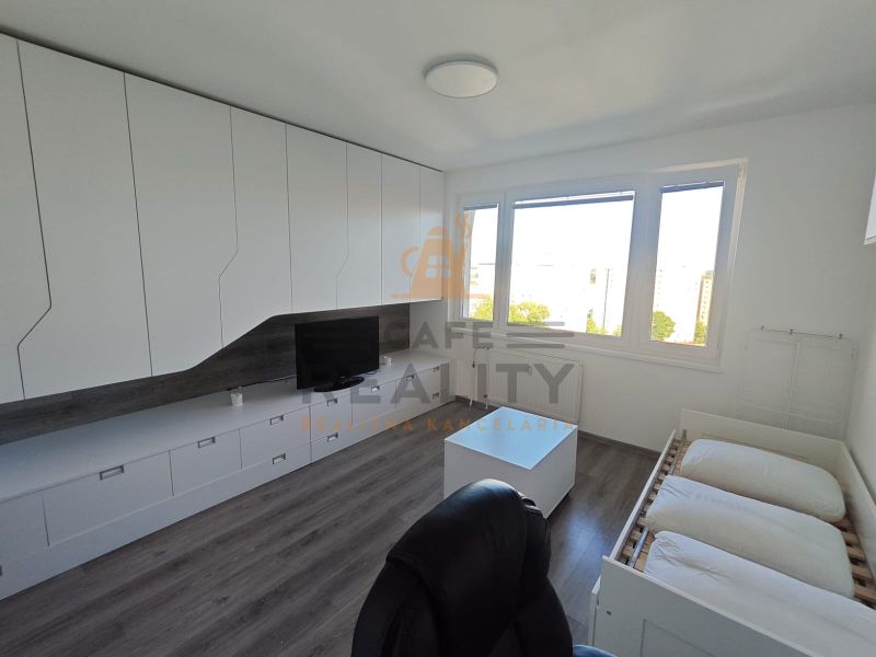 Na prenájom 1 izbový byt, 34 m2, Bratislava, Petržalka, Lachova ulica - Interiér 1-izbového bytu s bielymi skrinkami, podlahou s dreveným dekorom a veľkými oknami.