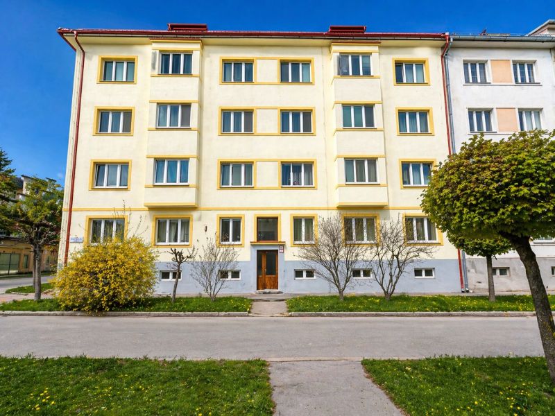 Na predaj priestranný 4-izbový byt - Robotnícka ulica, Banská Bystrica - Bytový dom v Banskej Bystrici, žltá fasáda, upravená zeleň, jasná obloha.