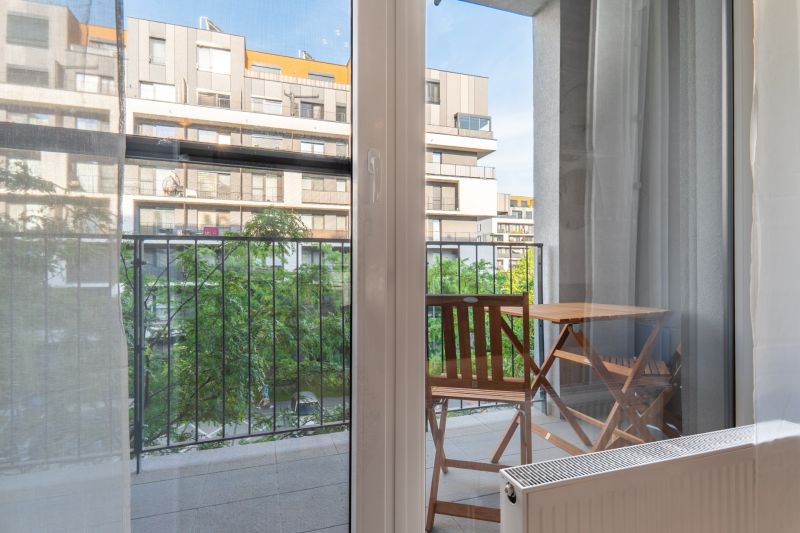I Slnečnice – Zóna mesto moderný 1-izb byt s loggiou - Výhľad z 1-izbového bytu na balkón so stolom a stoličkami.