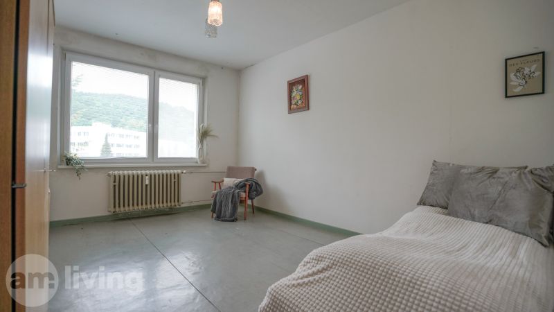 NOVINKA - 2 izbový + loggia + výťah v meste NOVÁ DUBNICA - Spálňa v 2-izbovom byte s veľkým oknom, kreslom a jednoduchým zariadením.