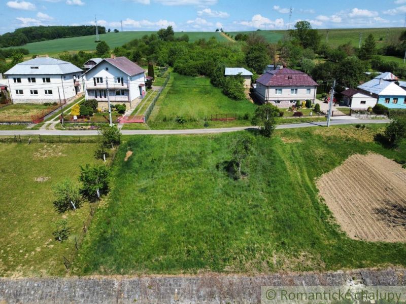 Slnečný stavebný pozemok 1 186 m² - Karná | možnosť dokúpiť 1 ha - Pozemky - bývanie v Karnej: zelené plochy, domy a príjazdová cesta pod modrou oblohou.