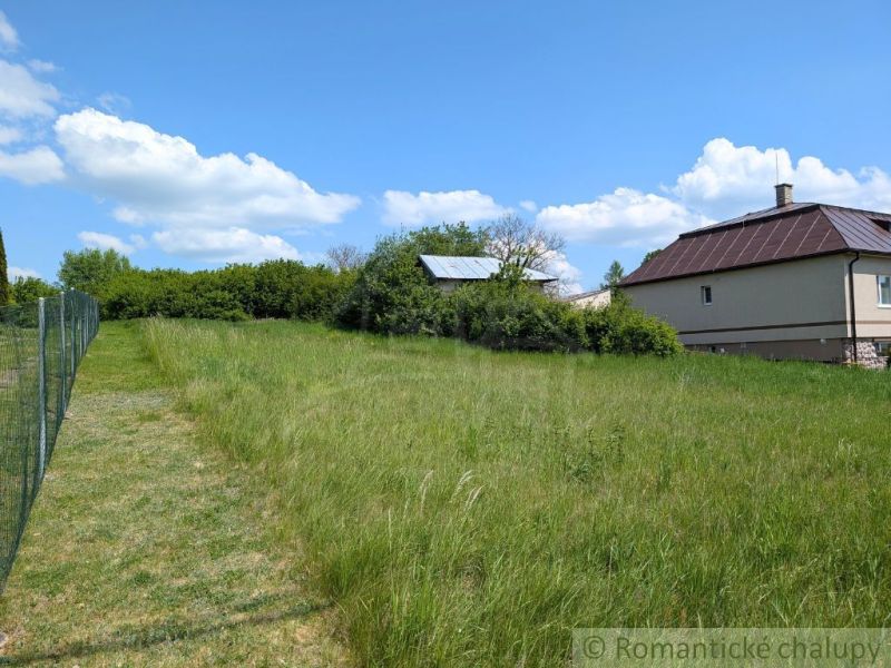 Slnečný stavebný pozemok 1 186 m² - Karná | možnosť dokúpiť 1 ha - Trávnaté pozemky na bývanie v Karnej s výhľadom na dom a modrú oblohu.