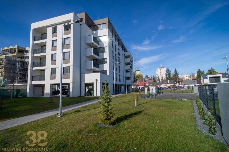 Lukratívny 2-izbový byt v Poprade na prenájom - Bytový dom v Poprade so zeleným trávnikom a susednými budovami v pozadí.