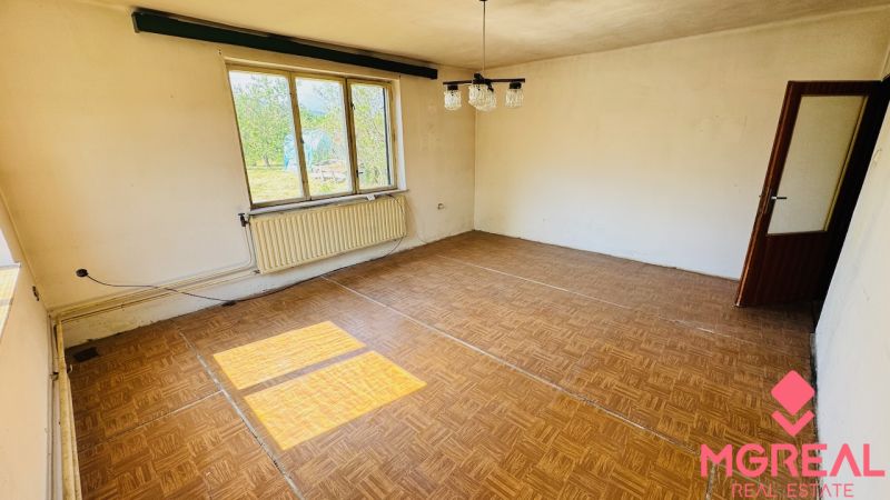 Na predaj 6-izbový rodinný dom (dvojdom) v Pažiti, pozemok 1445 m² - Izba s podlahou s dreveným dekorom, veľkým oknom a radiátorom v rodinnom dome.