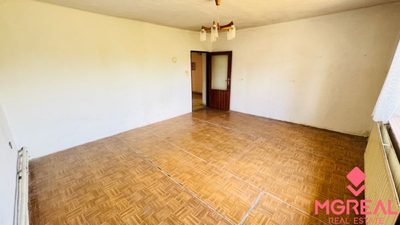 Na predaj 6-izbový rodinný dom (dvojdom) v Pažiti, pozemok 1445 m² - Izba v rodinnom dome s podlahou s dreveným dekorom a lustrom.