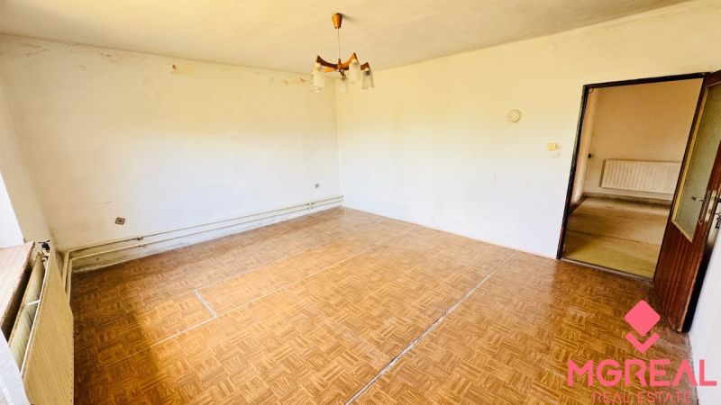 Na predaj 6-izbový rodinný dom (dvojdom) v Pažiti, pozemok 1445 m² - Obývačka v rodinnom dome s podlahou s dreveným dekorom a jednoduchým osvetlením.