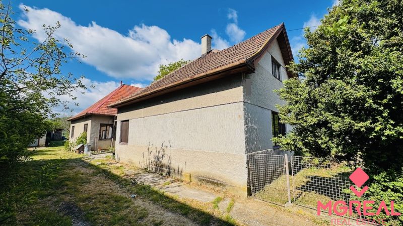 Na predaj 6-izbový rodinný dom (dvojdom) v Pažiti, pozemok 1445 m² - Rodinný dom v Pažiťi obklopený zeleňou, s červenou strechou a drevenými oknami.