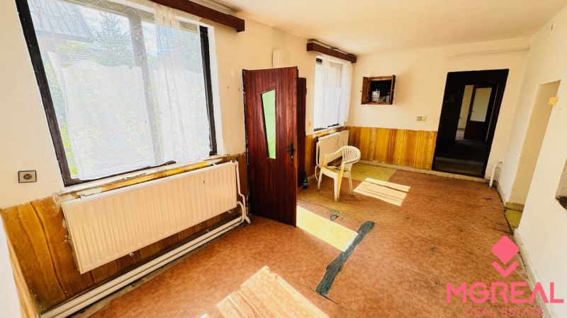 Na predaj 6-izbový rodinný dom (dvojdom) v Pažiti, pozemok 1445 m² - Interiér rodinného domu s otvorenými dverami, plastovými stoličkami a veľkými oknami.