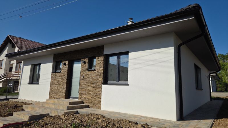 Bungalov v centre obce Cabaj Čápor, Wágnerova ulica, Dom č.1 - Rodinný dom v Cabaj-Čápore so svetlou fasádou a obkladom imitujúcim kameň.