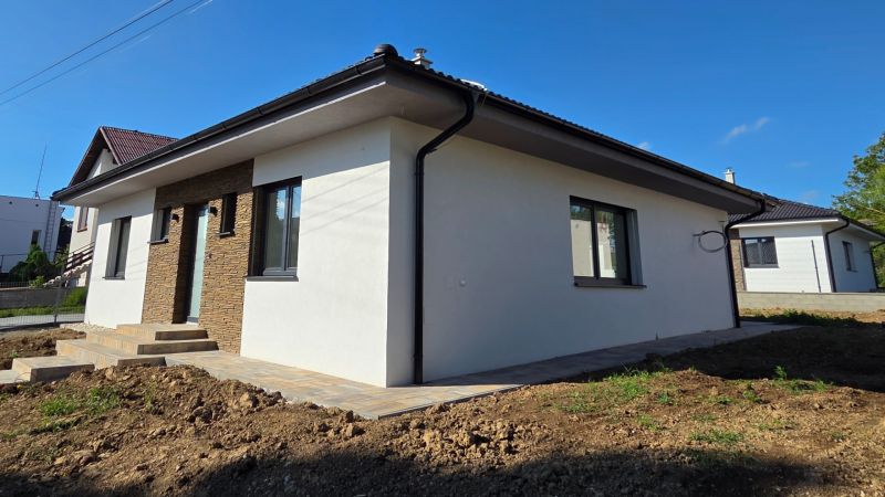 Bungalov v centre obce Cabaj Čápor, Wágnerova ulica, Dom č.1 - Rodinný dom v Cabaj-Čápore s bielou fasádou a kamennými obkladmi na vstupnej stene.