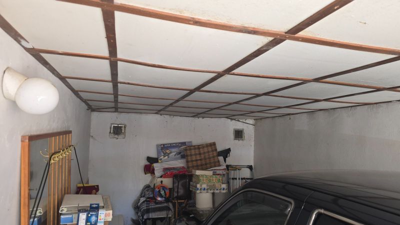 NA PREDAJ MUROVANÁ GARÁŽ 18 m² VO ZVOLENE – ELEKTRINA, VLASTNÝ POZEMOK - Garáže s bielym ventilátorom, uskladnenými vecami a zaparkovaným autom.