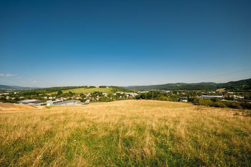 Na predaj stavebný pozemok pre rodinné domy – Banská Bystrica P306ZL - Krajina s trávnatou lúkou a dedinou na pozadí v okrese Banská Bystrica, Banskobystrický kraj, vhodná pre Pozemky - bývanie.