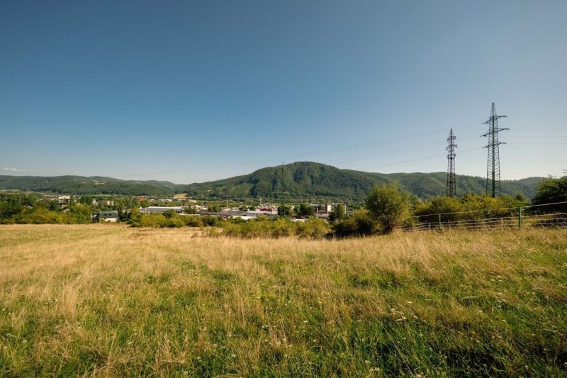 Na predaj stavebný pozemok pre rodinné domy – Banská Bystrica P306ZL - Krajina s trávnatým pozemkom a elektrickými stĺpmi na Partizánskej ceste, Banská Bystrica. Pozemky - bývanie.