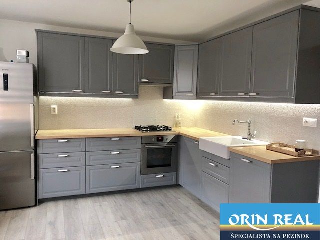 NA PRENÁJOM Pekný 2 izbový byt v Centre Pezinka 700,- EUR - Moderná kuchyňa v 2-izbovom byte so sivými skrinkami a podlahou s dreveným dekorom.