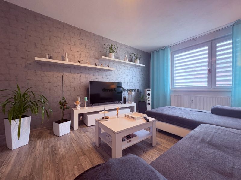 Na predaj: 4 izb.byt + BALKON + PIVNICA - Obývacia izba v 4-izbovom byte s podlahou s dreveným dekorom a sivými závesmi.