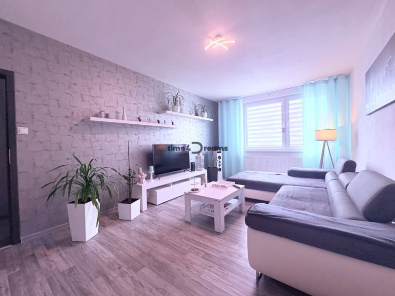 Na predaj: 4 izb.byt + BALKON + PIVNICA - Obývačka so sivou sedačkou, podlahou s dreveným dekorom a dekoratívnou tehlovou stenou v 4-izbovom byte.