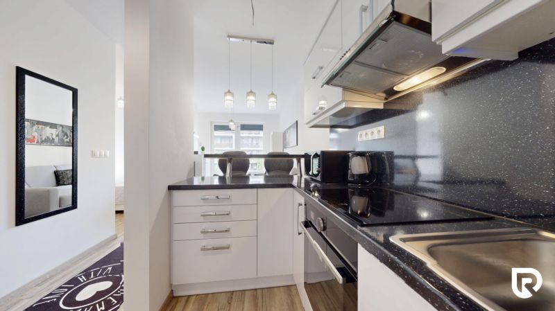 | Zariadený 1,5 izbový byt | 35m² | SLNEČNICE - Kuchyňa v 2-izbovom byte s lesklou pracovnou doskou a zrkadlom na stene.