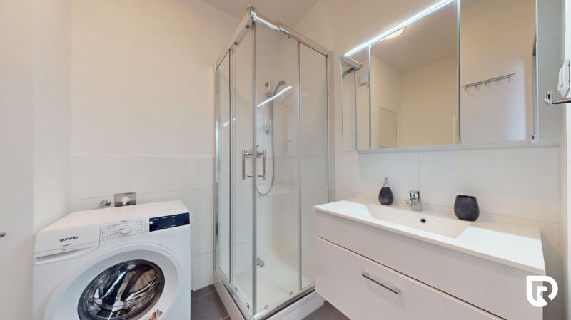 | Zariadený 1,5 izbový byt | 35m² | SLNEČNICE - Kúpeľňa v 2-izbovom byte s práčkou, sprchovým kútom a umývadlom s úložným priestorom.