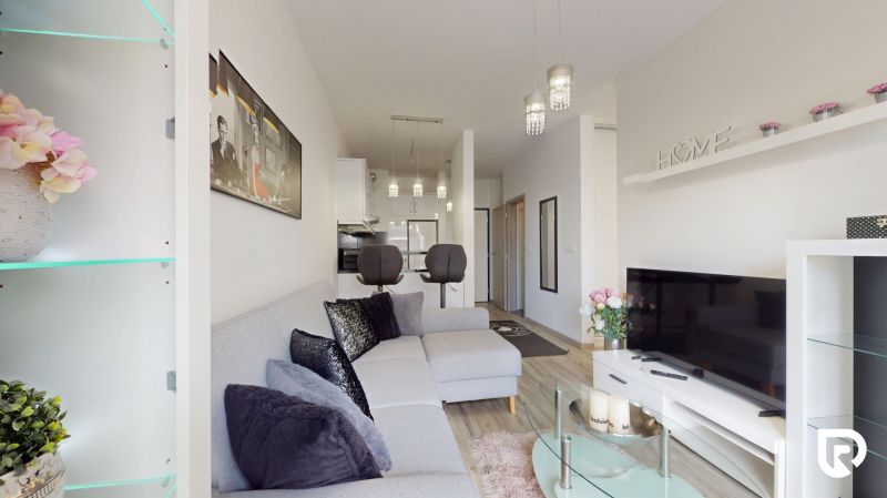 | Zariadený 1,5 izbový byt | 35m² | SLNEČNICE - Obývačka v 2-izbovom byte s pohovkou, televíziou a otvorenou kuchyňou.