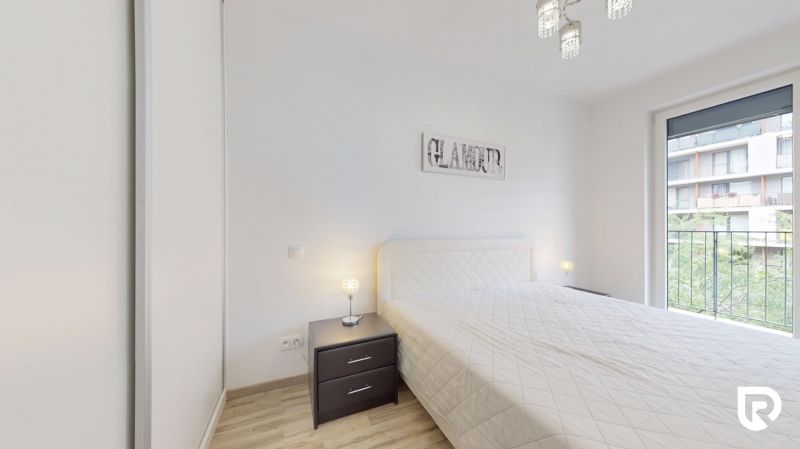 | Zariadený 1,5 izbový byt | 35m² | SLNEČNICE - Svetlá spálňa v 2-izbovom byte s posteľou, nočným stolíkom a balkónom.