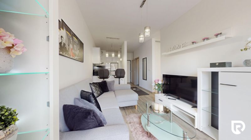 | Zariadený 1,5 izbový byt | 35m² | SLNEČNICE - Obývacia izba v 2-izbovom byte s pohodlnou sedačkou a vešiakom na stene.