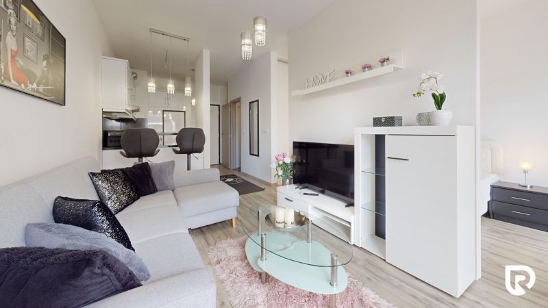 | Zariadený 1,5 izbový byt | 35m² | SLNEČNICE - Obývacia izba v 2-izbovom byte s pohovkou, televízorom a kuchyňou v pozadí.