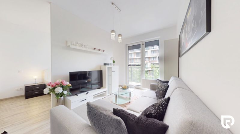 | Zariadený 1,5 izbový byt | 35m² | SLNEČNICE - Obývačka v 2-izbovom byte s pohovkou, televízorom a balkónovými dverami.
