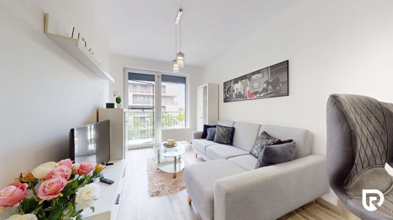 | Zariadený 1,5 izbový byt | 35m² | SLNEČNICE - Obývacia miestnosť s pohovkou a televízorom v 2-izbovom byte. Na stene visí dekorácia.