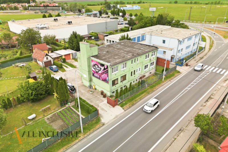 Na predaj veľkom. 3-izb. byt so záhradou, Veľký Meder - Ulica s budovami vo Veľkom Mederi, za ktorými sa rozprestiera zelená krajina.
