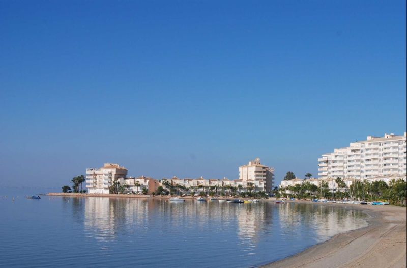 Predaj- Apartmány - La Manga del Mar Menor- Španielsko  - Pobrežie s rekreačnými apartmánmi v La Manga del Mar Menor pri pokojnom mori a modrej oblohe.