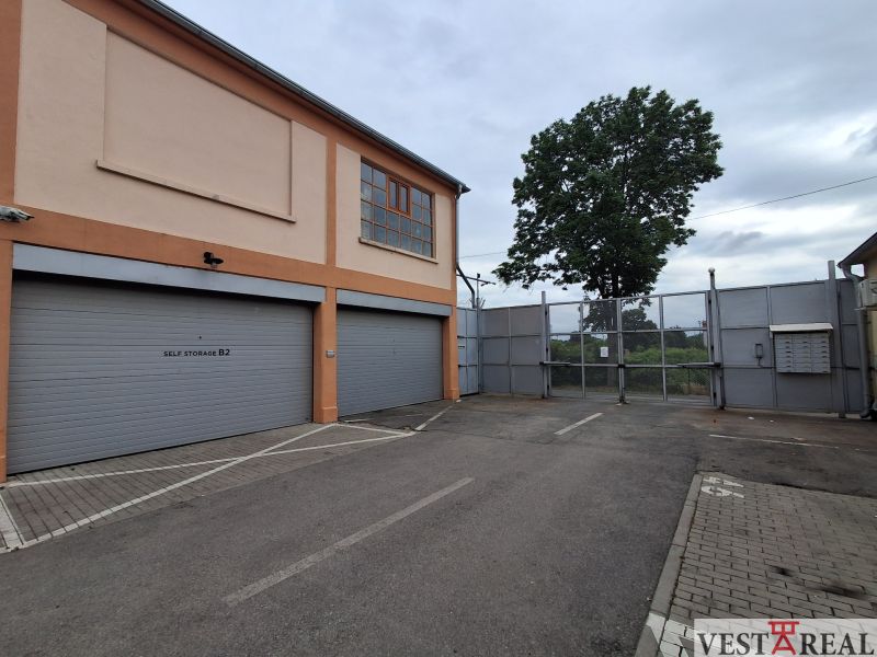 Na prenájom skladové priestory od 25 m2 Trnava Coburgova - Exteriér skladu a hál na Coburgovej ulici v Trnave, s veľkými bránami a stromom.