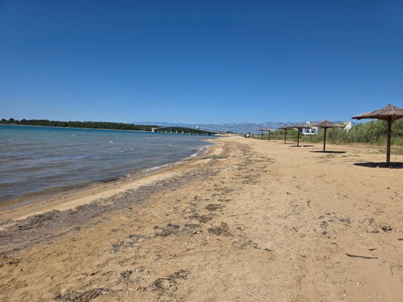 CHORVÁTSKO - Apartmány 60 m od mora - PRIVLAKA - Piesočná pláž s rákosovými slnečníkmi v Privlake, s modrou oblohou a morom.