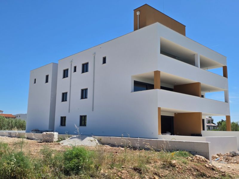 CHORVÁTSKO - Apartmány 60 m od mora - PRIVLAKA - Biely bytový dom s balkónmi v Privlake oproti modrej oblohe, 3-izbový byt.