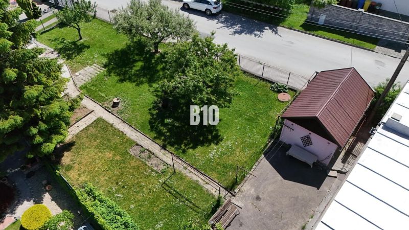 Dom STRÁNE s investičným pozemkom - Záhrada s trávnikom pri rodinnom dome v Martine, vidno strom, záhradnú cestu a prístrešok.