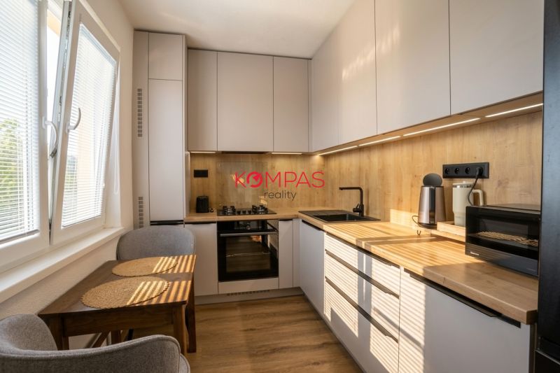 MODERNÝ  2-IZB.BYT PO KOMPLETNEJ REKONŠTRUKCII, UŽ LEN BÝVAŤ - Kuchyňa v 2-izbovom byte s dreveným dekorom skríň a kompaktným stolom.