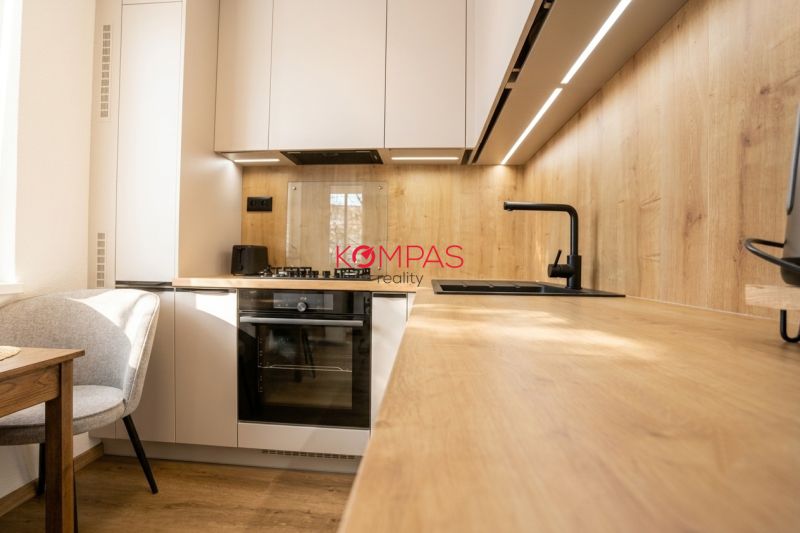MODERNÝ  2-IZB.BYT PO KOMPLETNEJ REKONŠTRUKCII, UŽ LEN BÝVAŤ - Kuchyňa v 2-izbovom byte s podlahou s dreveným dekorom, svetlými skrinkami a spotrebičmi.