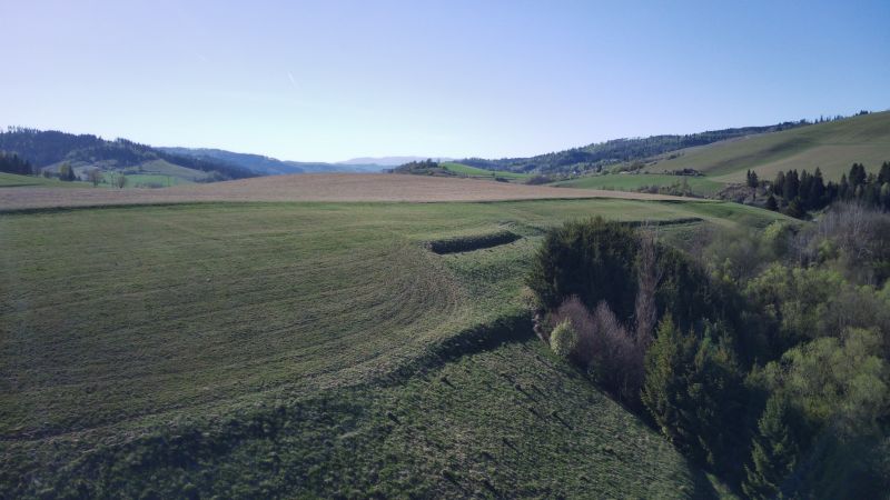 Čierny Balog – 338 m2 POĽNOHOSPODÁRSKY pozemok v 1/1 - Krajina v okolí Čierneho Balogu s poľnohospodárskymi a lesnými pozemkami, za jasného dňa.