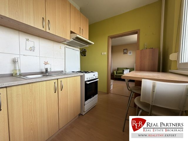 Predaj pekný 1 izbový byt, 35 m2, Dudvážska ulica, BA II. - Kuchyňa v 1-izbovom byte s podlahou s dreveným dekorom, jedálenský stôl a vybavenie.