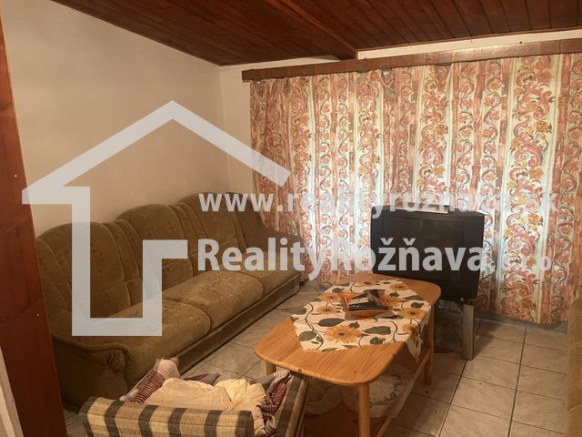 PREDAJ/ Krásna chalupa s vinicou/Jablonov nad Turňou - Obývacia miestnosť v chate s pohovkou, kreslom, televízorom a kvetinovým závesom.