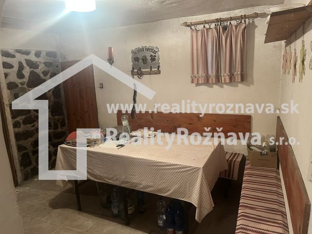 PREDAJ/ Krásna chalupa s vinicou/Jablonov nad Turňou - Jedálenský kút s obrusom, lavicou a kameňom na stene v chate.