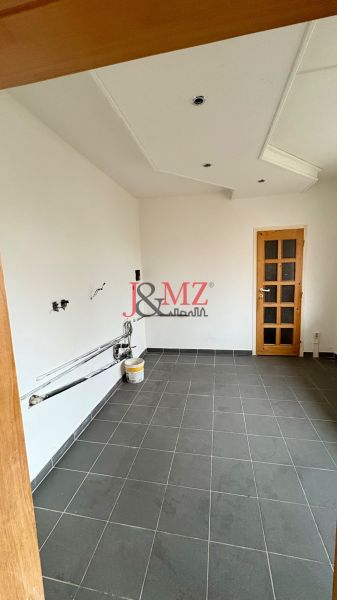 Slnečný 2-izbový byt vo vynikajúcej lokalite – stačí dokončiť kuchyňu  - Prázdna miestnosť v 2-izbovom byte, podlaha z tmavej dlažby, biele steny, drevené dvere.