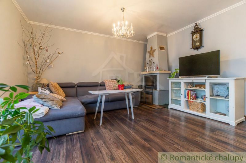 Komfortný dom v pokojnej záhradkárskej oblasti v Bernolákove - Obývačka v rodinnom dome s krbom, rohovou sedačkou a podlahou s dreveným dekorom.