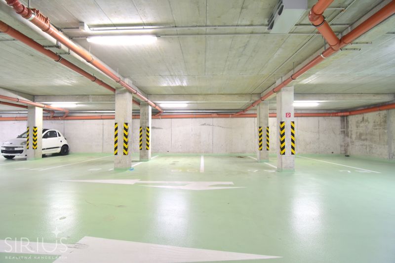 UZBECKÁ, parkovacie miesto v garáži, novostavba Oppidum - Podzemné garáže s parkovacím miestom, zelenou podlahou a oranžovým potrubím.