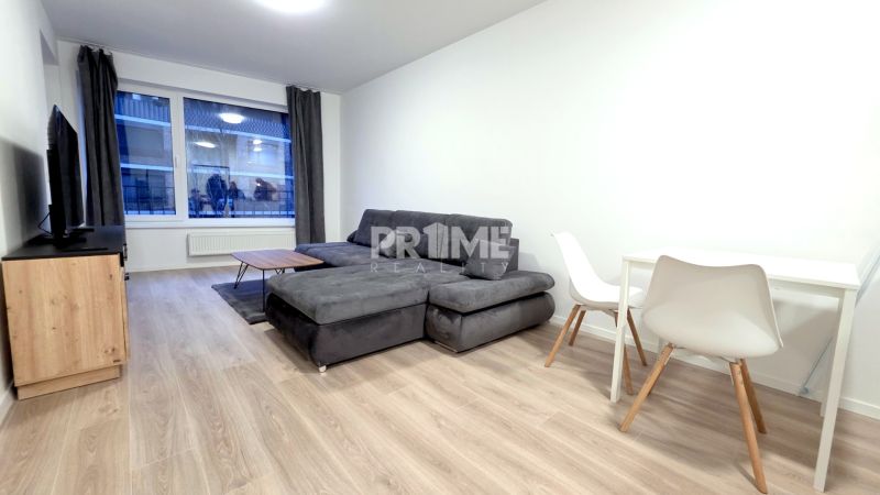 U NÁS !!! MODERNÝ 2i,NOVOSTAVBA, LOGGIA, Slnečnice UNIQ, Fialova ulica - Svetlá obývacia izba s podlahou s dreveným dekorom a sivou sedačkou v 2-izbovom byte.
