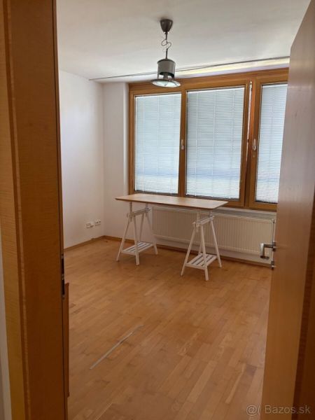4 izbový byt 120 m2 Ružová dolina, Ružinov, 1x podzemné´parkovanie - Miestnosť s veľkým oknom, stolom a podlahou s dreveným dekorom v 4-izbovom byte.