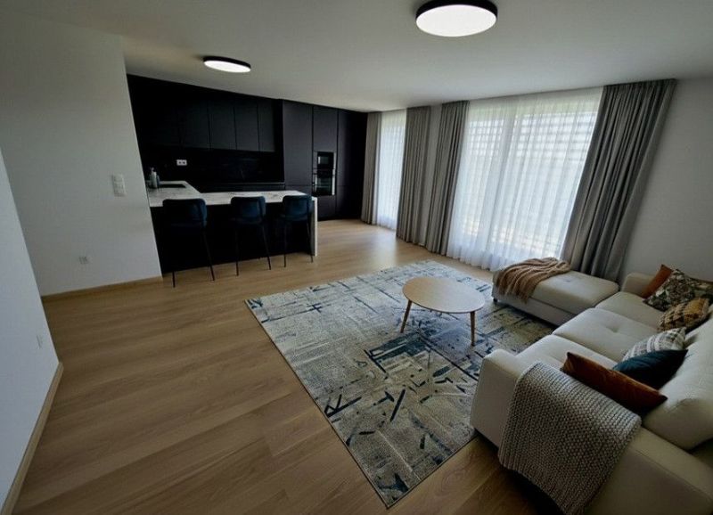 PREDAJ ELEGANTNÝ 2-IZBOVÝ BYT S BALKÓNOM A PARKOVANÍM V RAČI - Obývacia izba v 2-izbovom byte s podlahou s dreveným dekorom a svetlým nábytkom.