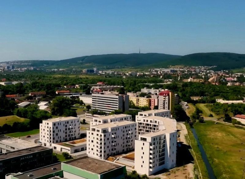 PREDAJ ELEGANTNÝ 2-IZBOVÝ BYT S BALKÓNOM A PARKOVANÍM V RAČI - Pohľad na obytné budovy a okolitú zeleň v Bratislave III, vhodné pre 2-izbový byt.