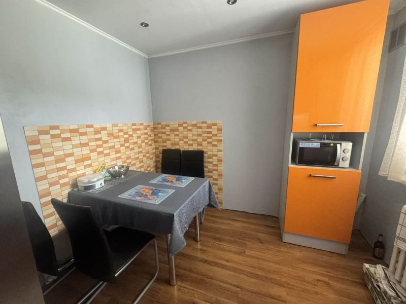 3 izbový byt 75m2, ul.Bruselská, Košice- Ťahanovce - Kuchyňa s oranžovou kuchynskou linkou, jedálenským stolom a podlahou s dreveným dekorom.