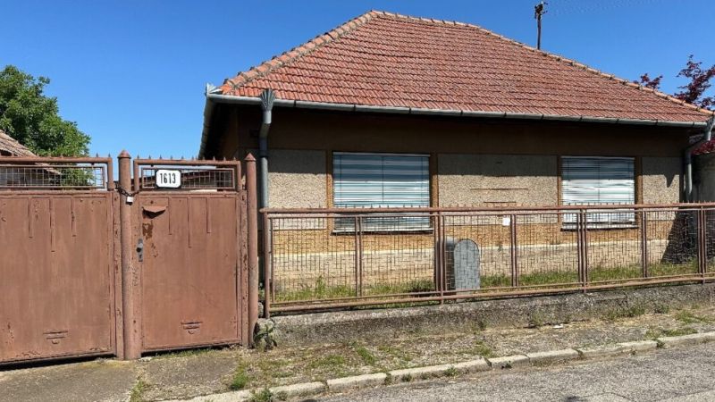 Na predaj rodinný dom s veľkým pozemkom v tichej lokalite - Rodinný dom v Močenku s hnedou bránou a šikmou strechou.